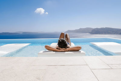 Woman relaxing in swimming pool by sea against sky