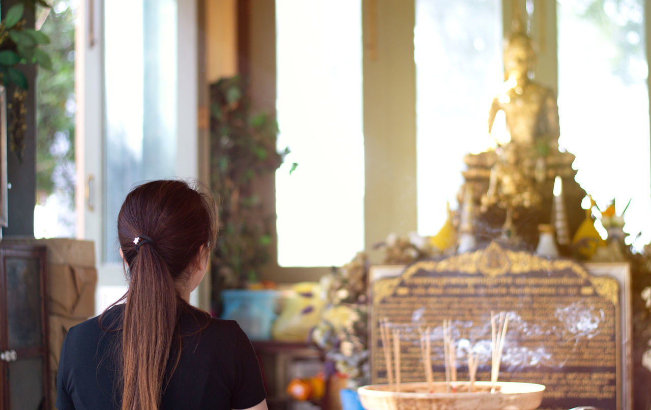 REAR VIEW OF WOMAN SITTING AT HOME