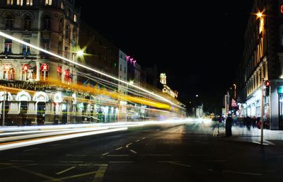 Light trails on city street amidst buildings at night