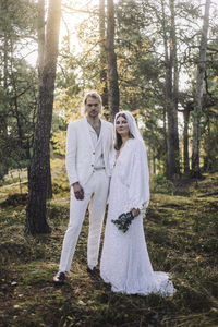 Portrait of well dressed bride and groom standing by trees in forest at wedding