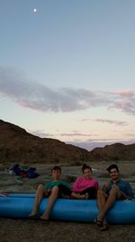 Friends sitting on land against sky during sunset