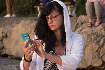 Portrait of beautiful woman with hood at sunrise light, using smart phone