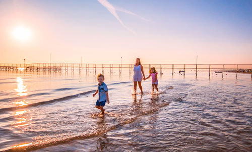 Mother with children walking in sea on shore at beach during sunset