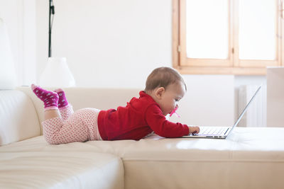 Baby girl using laptop while lying on bed at home