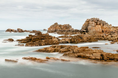 Rock formations at beach against cloudy sky