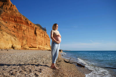 Full length of man on rock in sea against clear sky