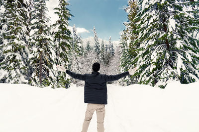 Rear view of mature man with arms outstretched standing in forest during winter