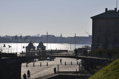 People on bridge over river against buildings in city