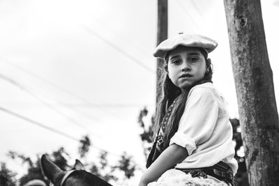 Low angle portrait of girl riding horse against clear sky