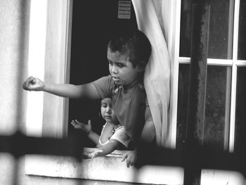 Siblings looking through window and playing at home