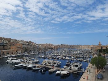 Sailboats moored in harbor by city against sky