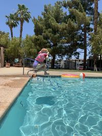 Woman jumping in swimming pool against trees