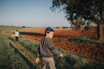 REAR VIEW OF MAN STANDING ON FIELD AGAINST CLEAR SKY