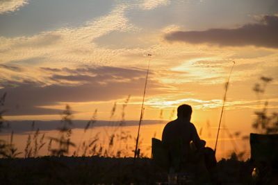 Silhouette man sitting against orange sky