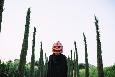 Anonymous person wearing spooky halloween pumpkin mask and black cloak standing on sandy road