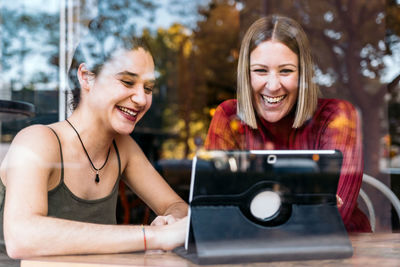Two young women are using a tablet in a coffee shop. 