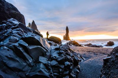 Silhouette rocks on beach against sky during sunset