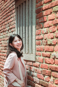 Portrait of smiling woman standing against brick wall