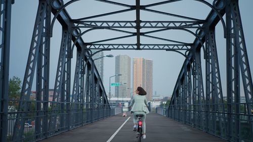 Back view of the businesswoman commuter on the way to work through the bridge using bicycle