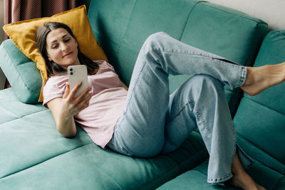 A woman lying on a sofa uses a phone for video calling.