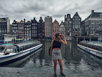 Woman standing by canal in city against sky