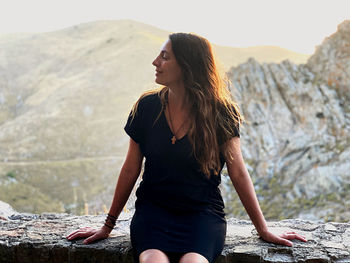 Young woman looking away while sitting on rock