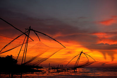 Silhouette fishing nets on sea against sky during sunset