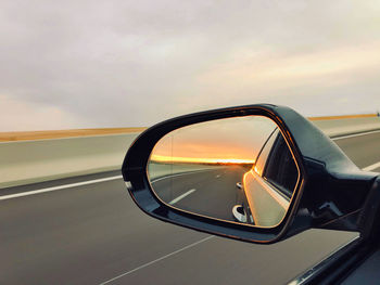 Close-up of side-view mirror against sunset sky