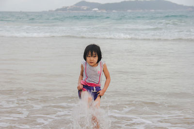 Full length of girl splashing water at beach against sea