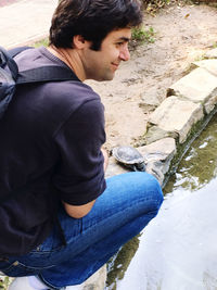 Side view of young man sitting by water