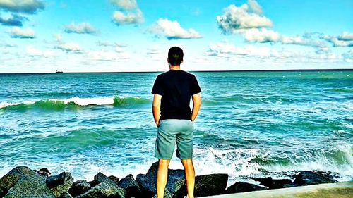 Rear view of man standing on beach against sky