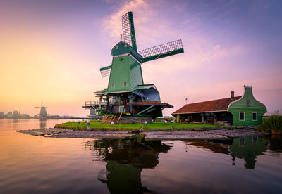 Traditional windmill by building against sky during sunset
