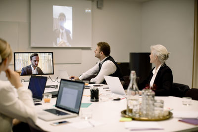 Male and female business professionals discussing in global video conference at board room