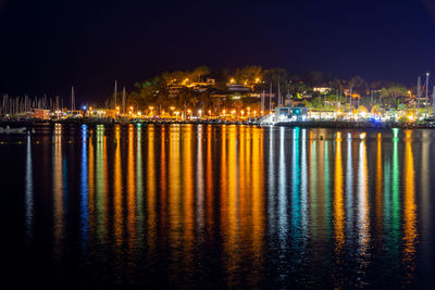 Illuminated city by sea against sky at night