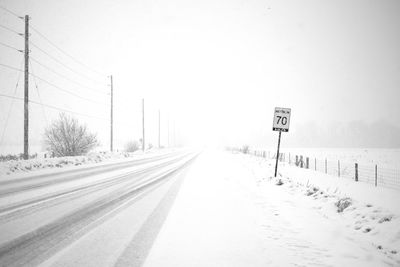 Road sign on snow covered landscape against clear sky