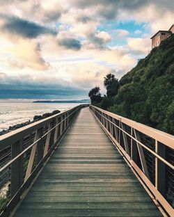 Footbridge by mountain against cloudy sky during sunset