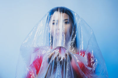 Young woman wrapped in plastic holding crystal ball against blue background