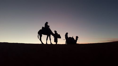 Silhouette people on desert against sky during sunset