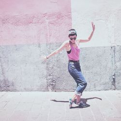 Full length of happy young woman dancing on footpath by wall