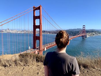 Rear view of man looking at suspension bridge against sky