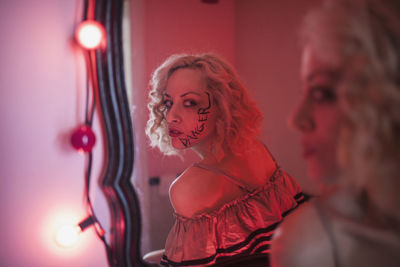 A young woman in a mirror with writing on her face.