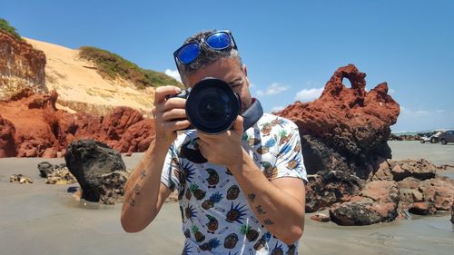 Man photographing on rock against sky