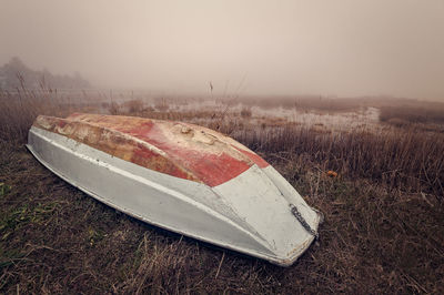 Upside down image of abandoned boat on field against sky