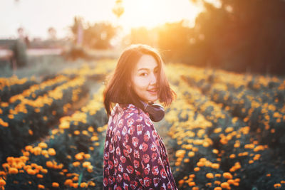 Portrait of beautiful young woman standing on field during sunset