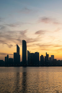 Sea by buildings against sky during sunset