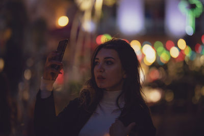 Beautiful woman taking selfie in illuminated city at night