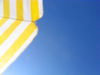 Low angle view of yellow flag against clear blue sky