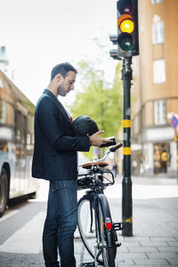 Side view of businessman using mobile phone while standing with bicycle on city street