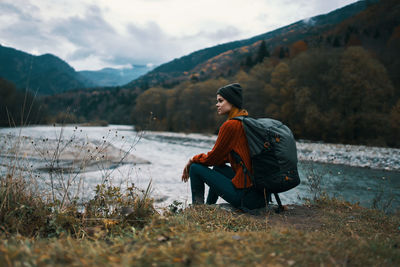 Woman sitting on shore against mountains