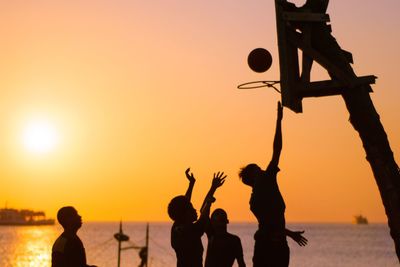 Silhouette men with arms outstretched against sky during sunset